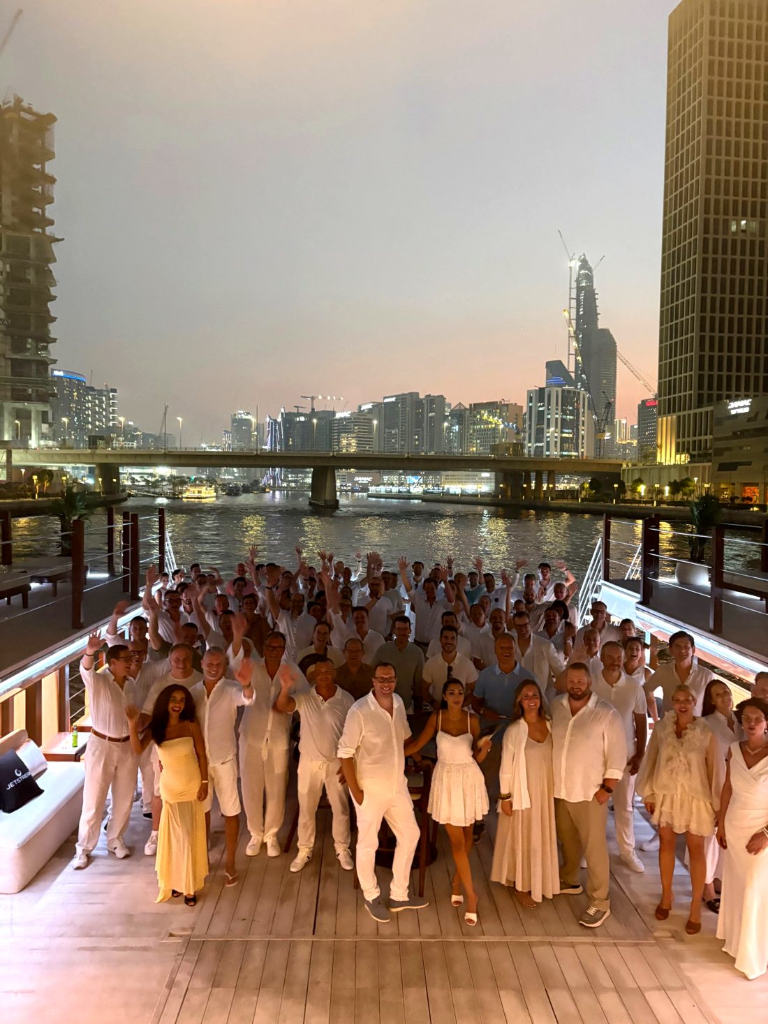 Jetstream members dressed in white on the deck of a houseboat on the Dubai Canal at dusk