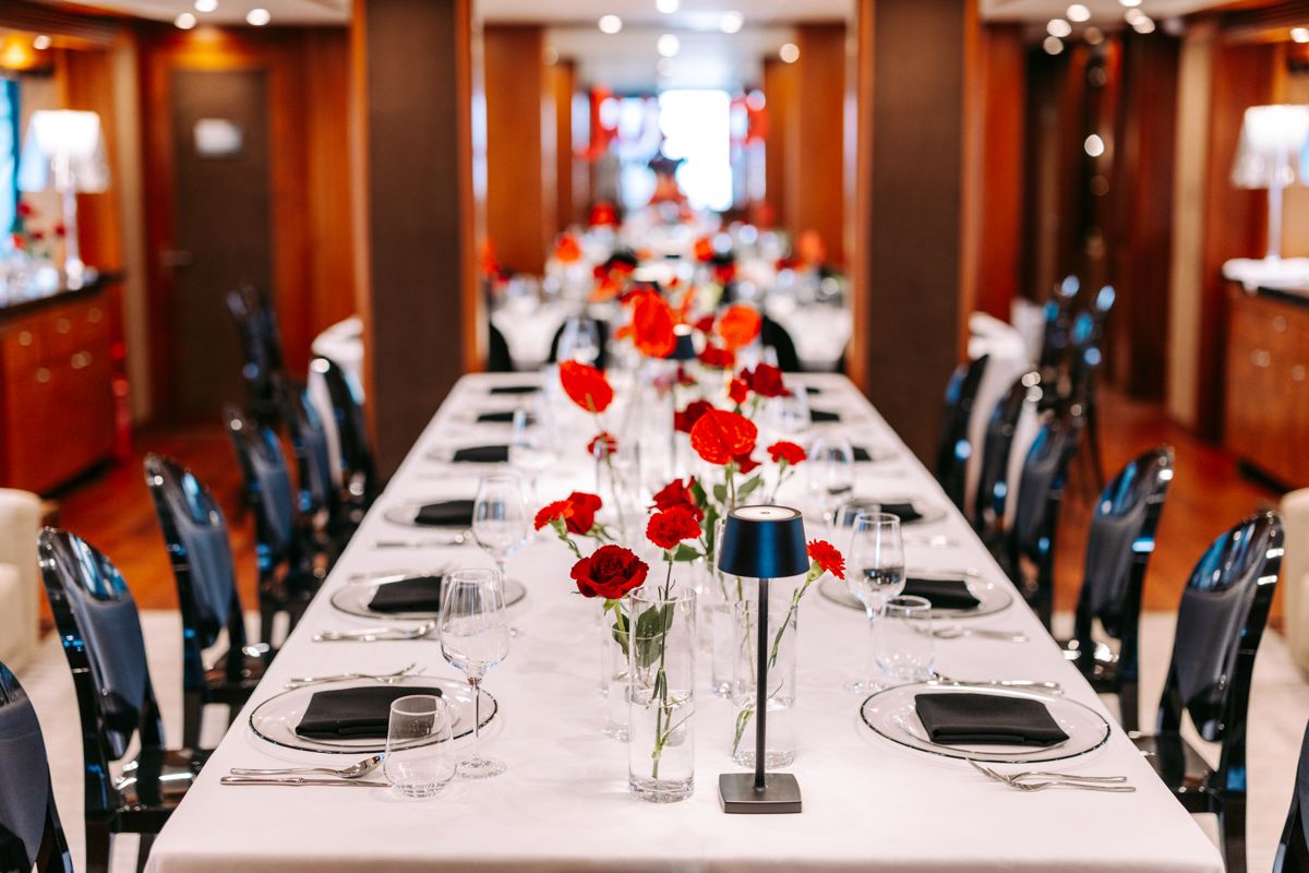 A long table dressed in white linen and red roses in the saloon of a superyacht