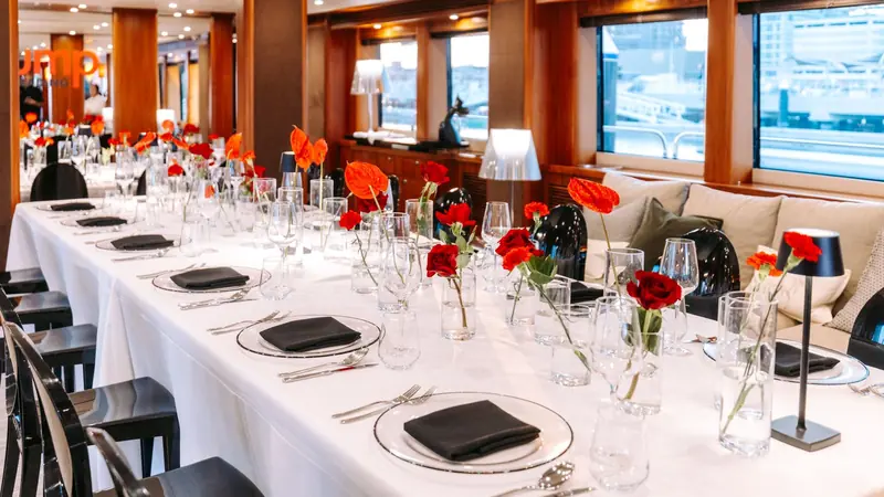 Main deck saloon of a superyacht set for a corporate seated dinner with white linen and red roses